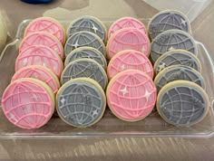 some cookies that are sitting in a plastic container on a table and one is decorated with pink, grey and white icing