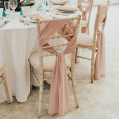 the table is set with white linens and pink sashes on it's chairs