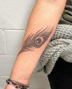 a woman's arm with a black and grey feather tattoo on the left forearm