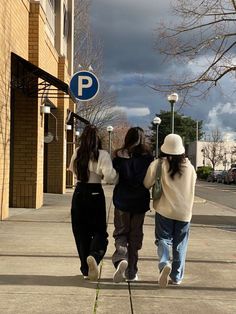 three girls walking down the street in front of a parking sign with a cloudy sky behind them