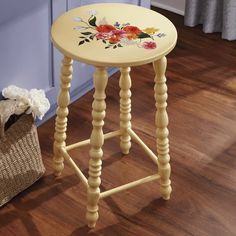 a yellow stool with flowers painted on the top and bottom, next to a basket