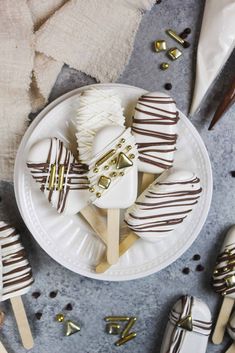 chocolate covered marshmallow pops on a white plate with gold decorations and forks next to them