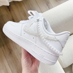 a person holding up a white nike air force shoe with pearls on the soles