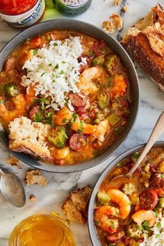 two bowls filled with shrimp and rice next to bread on a marble counter top,