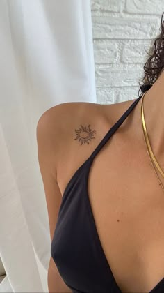 a woman with a tattoo on her chest wearing a black tank top and gold necklace