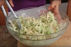 a person is mixing up some food in a glass bowl on the counter top with two tongs