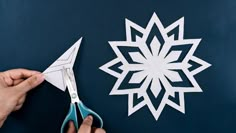 someone cutting out a paper snowflake on a blue surface with scissors and pliers