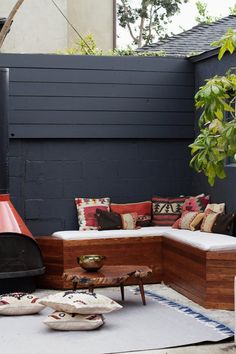 an outdoor seating area with lots of pillows on the couch and rugs around it