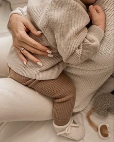 a woman holding a baby in her arms on top of a white bed next to shoes