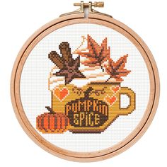 a cross stitch pattern with autumn leaves and a cup of coffee on the front, in a wooden frame