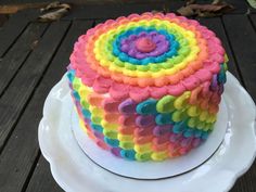 a multicolored cake sitting on top of a white plate next to a wooden table