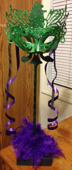 a purple and green mask on top of a wooden table next to a ribbon streamer