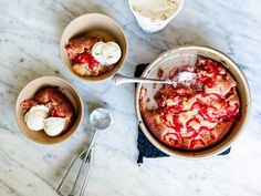 two bowls filled with cake and ice cream on top of a marble table next to spoons