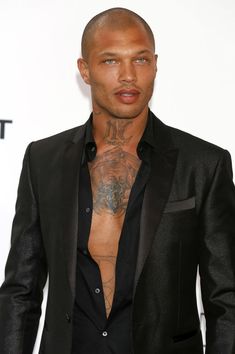 a man with tattoos on his chest wearing a suit and black shirt, standing in front of a white background