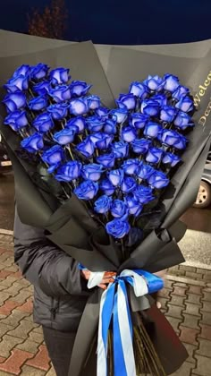 a woman holding a bouquet of blue roses in her hands with a heart shaped arrangement