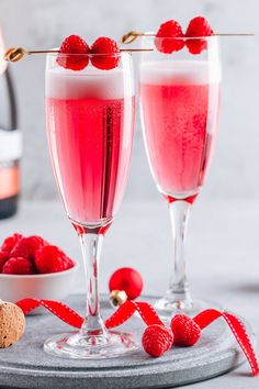 two glasses filled with raspberry champagne next to a bowl of raspberries