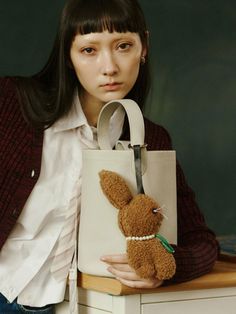 a woman holding a stuffed animal in front of her face and wearing a white bag