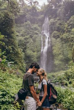 a man and woman standing in front of a waterfall with their backs to each other