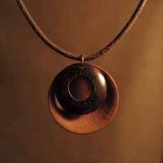 a necklace with a wooden disc hanging from it's end on a leather cord