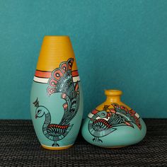 two vases sitting next to each other in front of a blue wall with a bird painted on it