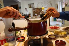 two people preparing food on a table with bowls and saucers around them, one person is holding a spoon in the other hand