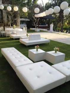 an outdoor seating area with white couches and flowers on the grass in front of it