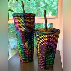 two colorful cups with straws in them sitting on a table next to a window