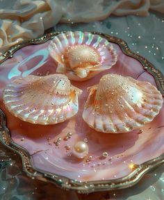 three seashells on a pink glass dish with water droplets and pearls around them