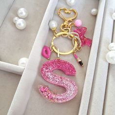 a pink and gold letter charm sitting in a white box next to pearl necklaces