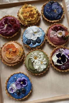 nine pies with flowers on them sitting in a cardboard box, ready to be eaten