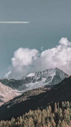 an airplane is flying in the sky over some trees and mountains with snow on them