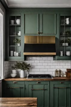 a kitchen with green cabinets and white subway backsplashes, brass range hood over the stove