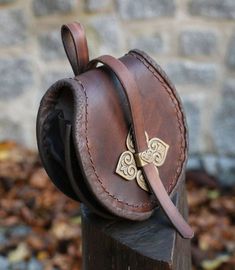 a brown leather bag with gold accents sitting on top of a wooden post