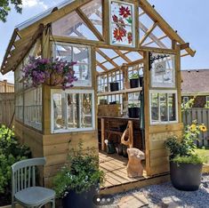 a small wooden house with lots of windows and plants in the front yard, along with potted flowers