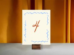 a piece of paper with the letter h on it sitting in front of a yellow curtain