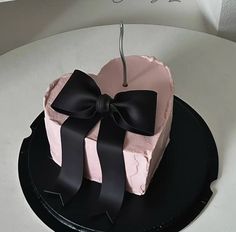 a pink and black heart shaped cake with a bow on the top sitting on a plate