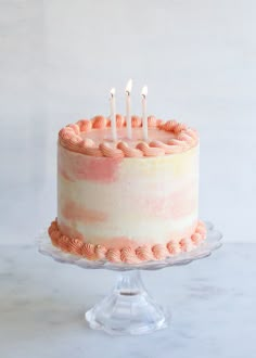 a cake with pink icing and five candles on top of it, sitting on a glass pedestal