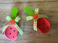 two paper strawberries with bows on them sitting on top of a wooden table next to each other