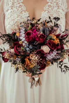 a woman holding a bouquet of flowers in her hands and wearing a wedding dress with lace sleeves