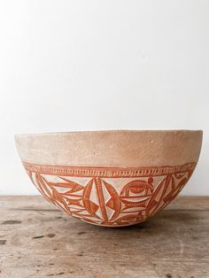 an orange bowl sitting on top of a wooden table next to a white wall and floor