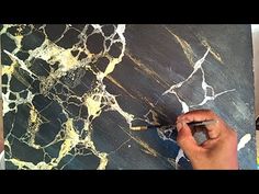 a man is painting on a black and gold marbled surface with paintbrushes