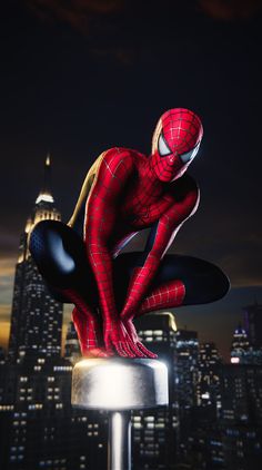 the amazing spider - man is posed on top of a pole in front of a cityscape