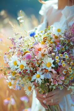 a woman holding a bouquet of wildflowers and daisies in her hands on a sunny day