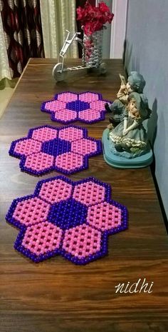 three pink and purple flower shaped rugs sitting on top of a wooden table next to a vase