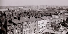 black and white photograph of an old city with tall buildings in the foreground, cars parked on the street