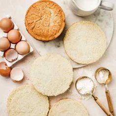 an assortment of bread, eggs and flour on a white counter top with measuring spoons