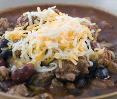 a close up of a bowl of chili with cheese on top and beans in it