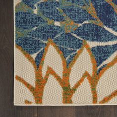 a blue and orange area rug with flowers on the floor in front of a wooden wall