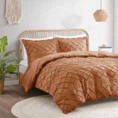 a bed with an orange comforter and pillows in a room next to a potted plant