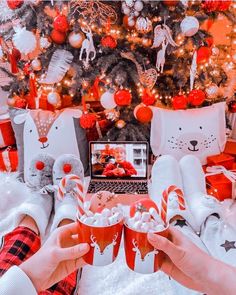 two people are holding cups with candy canes in front of a christmas tree